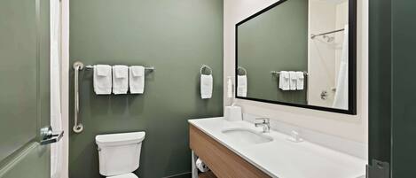 Un baño moderno con pared verde, accesorios blancos y un espejo grande.