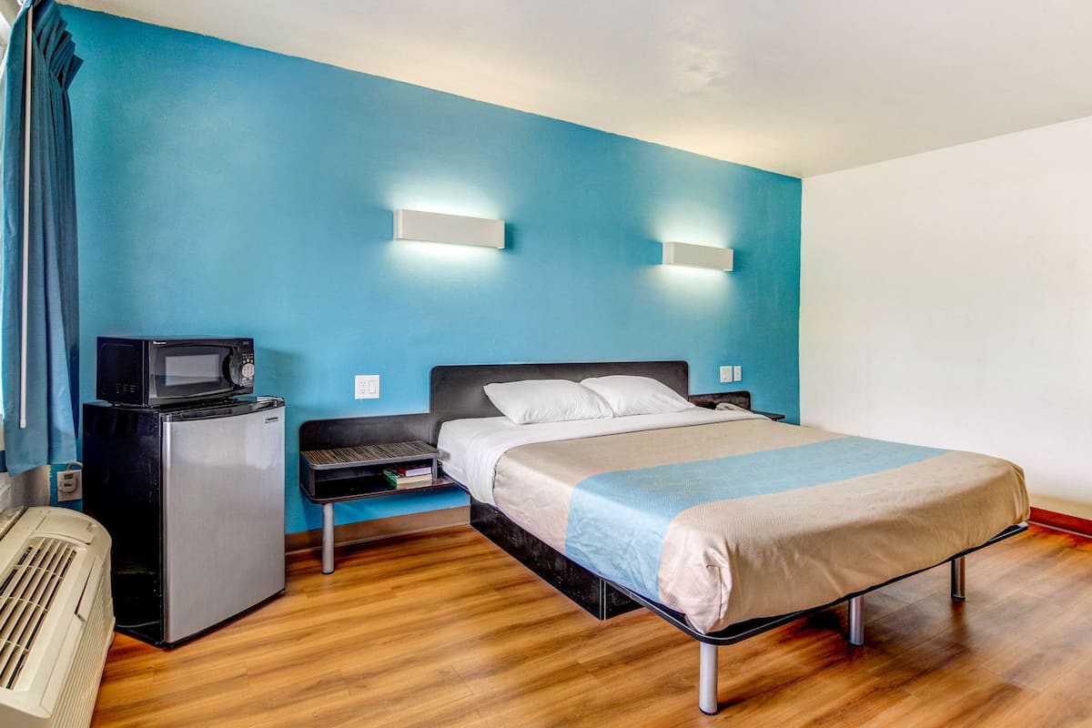 A hotel room with a bed, a small desk with a computer, a microwave, and a refrigerator.