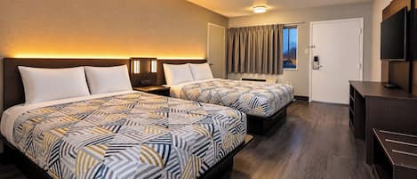 Una habitación de hotel con dos camas, un escritorio, un televisor y una ventana con cortinas.