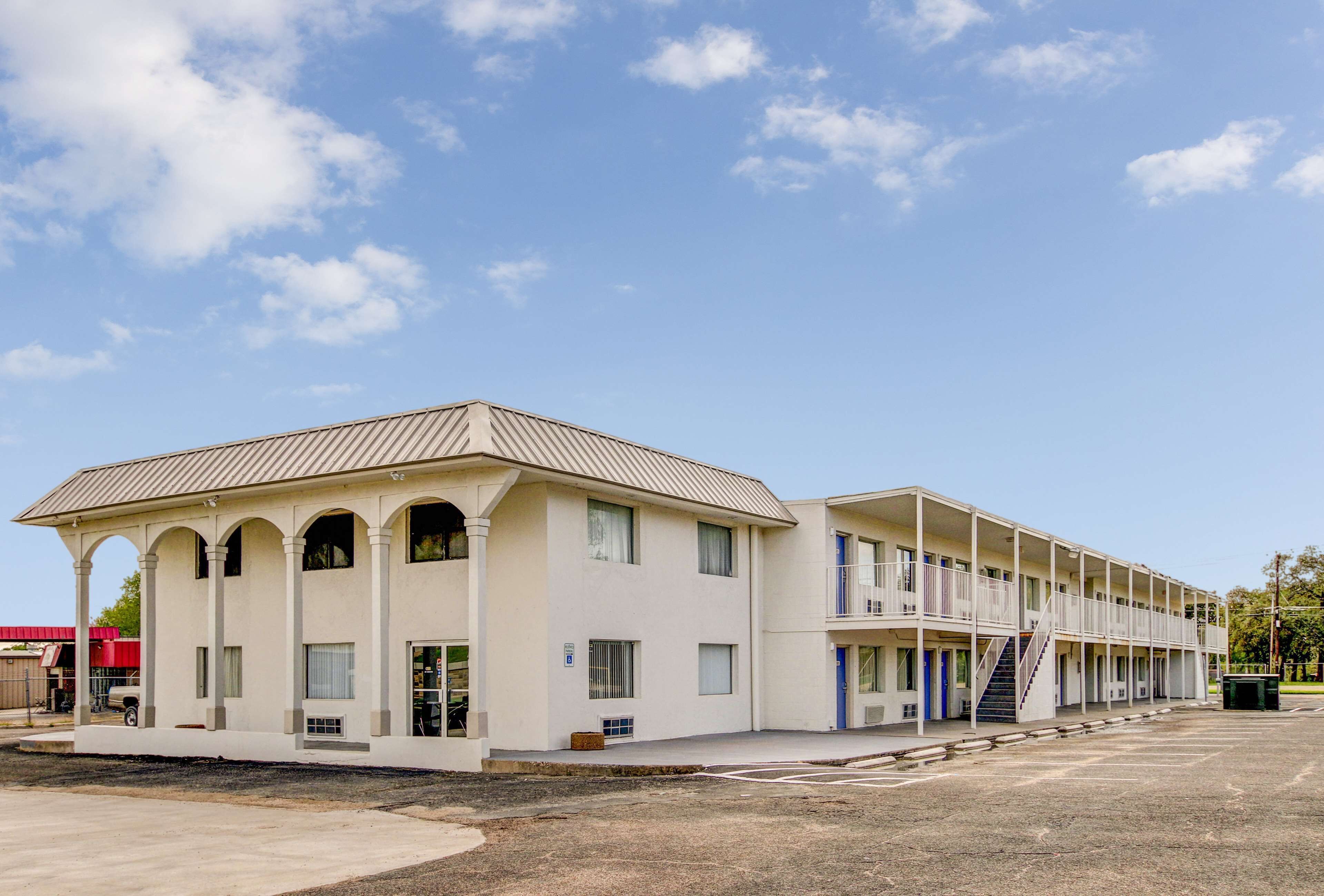 Un motel con una estructura de dos pisos, varios balcones y un área de estacionamiento techada.