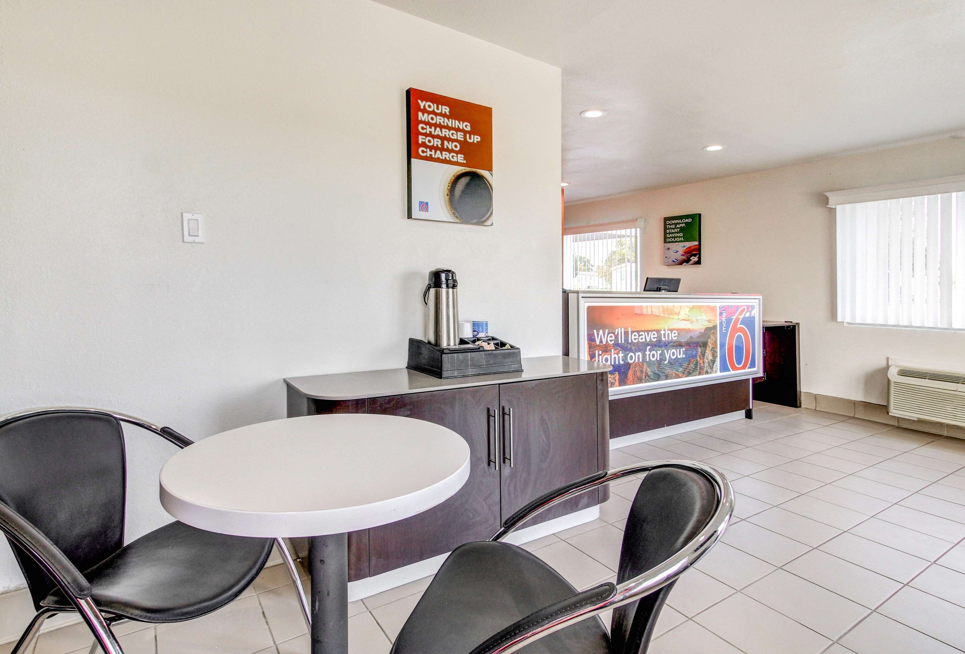A reception area with a round table, two chairs, a coffee machine, and a TV displaying a message.