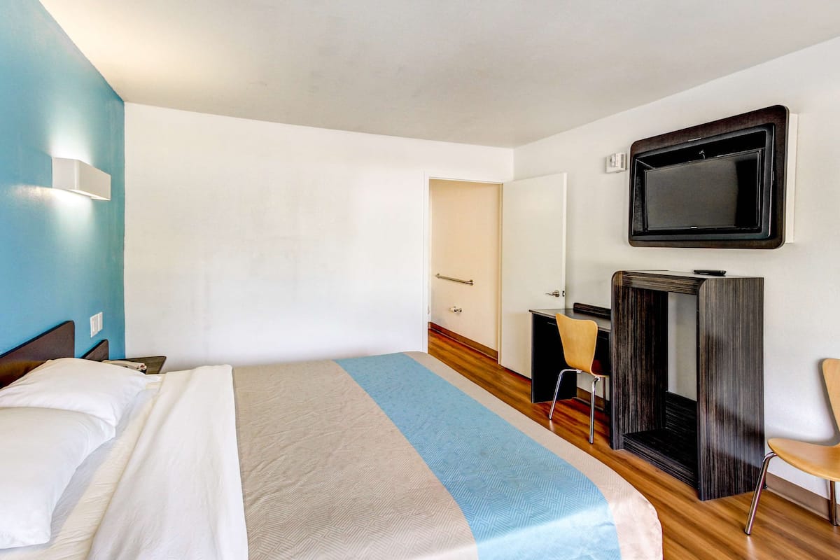 A hotel room with a bed, a desk, a chair, and a television on the wall.