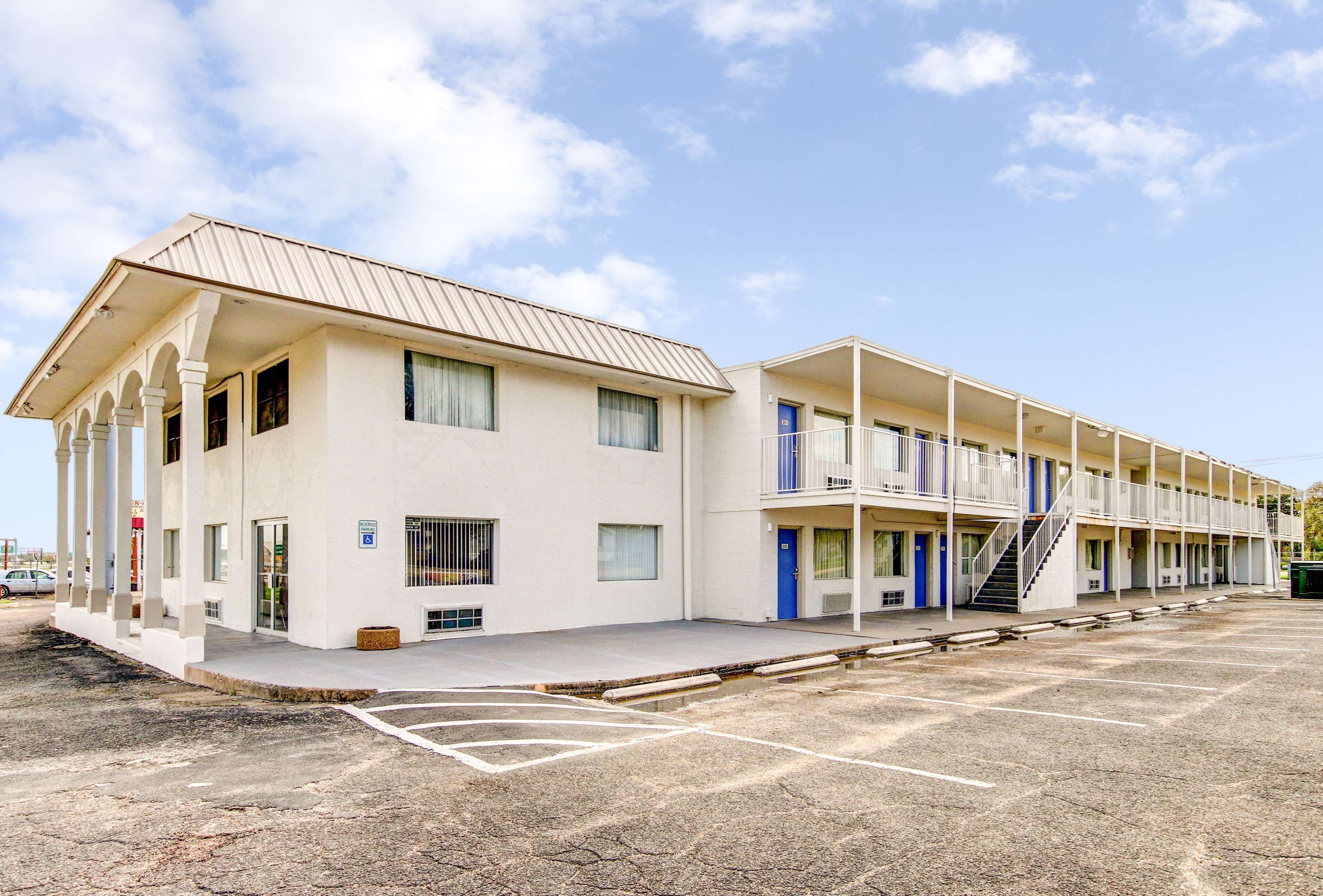 A motel with a two-story structure, a covered parking area, and a clear sky.