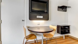 A small, modern room with a round table, two chairs, a mounted TV, and a small black shelf. - Motel 6 Waco, TX - Lacy Lakeview (Waco)
