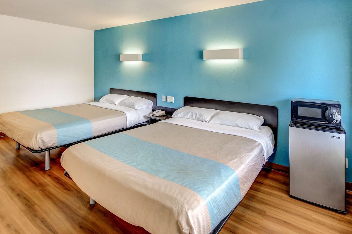 A hotel room with two beds, a small refrigerator, and a wall-mounted microwave.