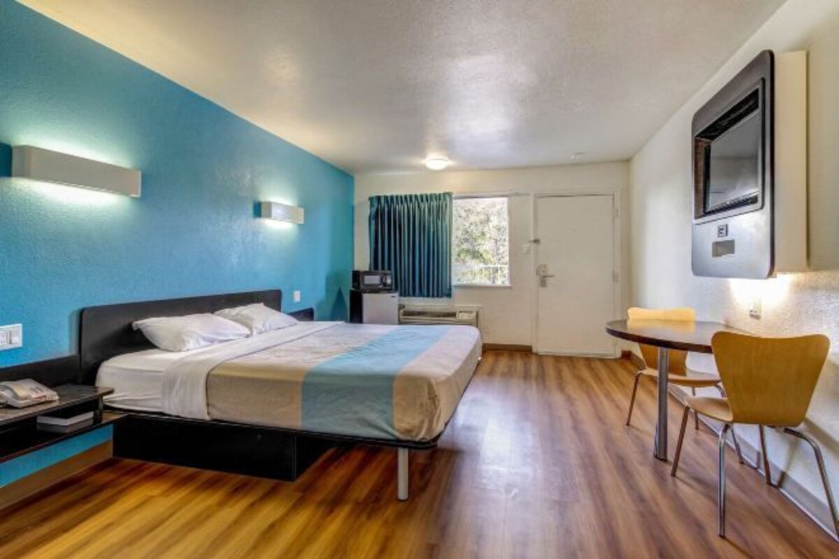 A hotel room with a bed, bedside table, lamp, and a small table with chairs.