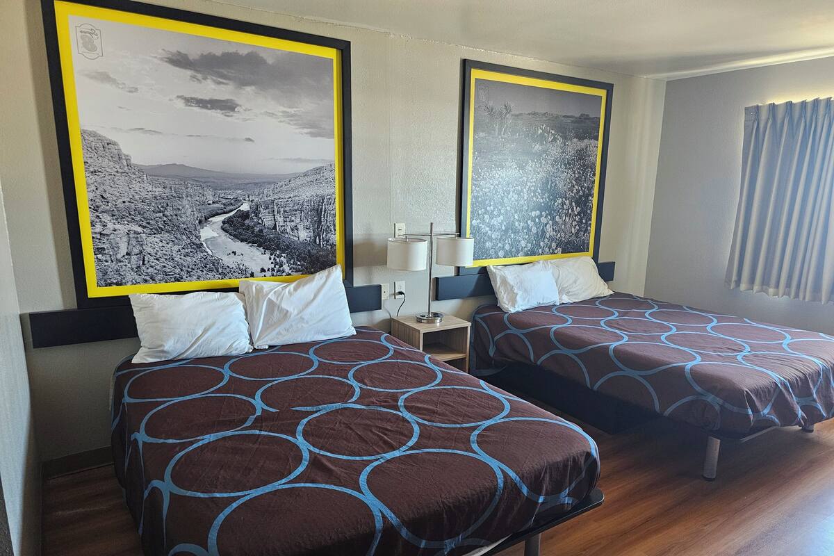 A hotel room with two beds, each with a patterned bedspread, a nightstand with a lamp, and two large framed pictures on the wall.