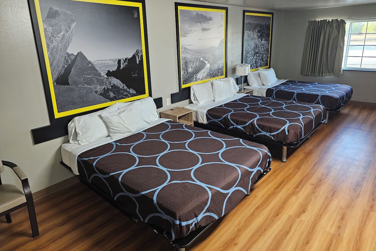 A hotel room with two beds, a wooden floor, and large landscape posters on the walls.