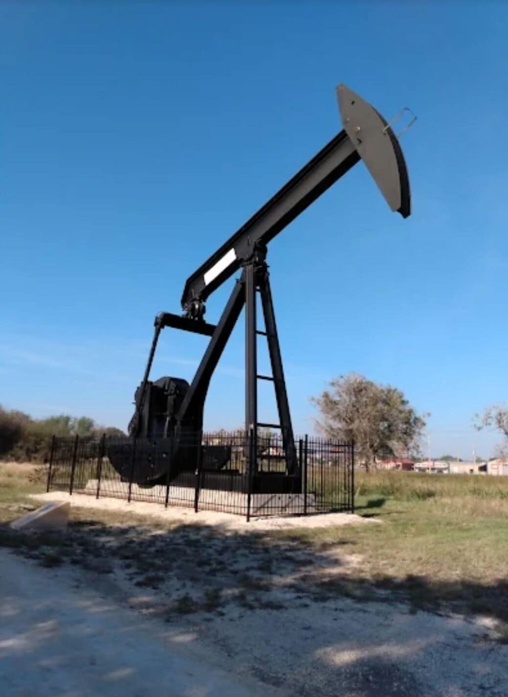 An oil pump jack in a fenced area with a clear sky.