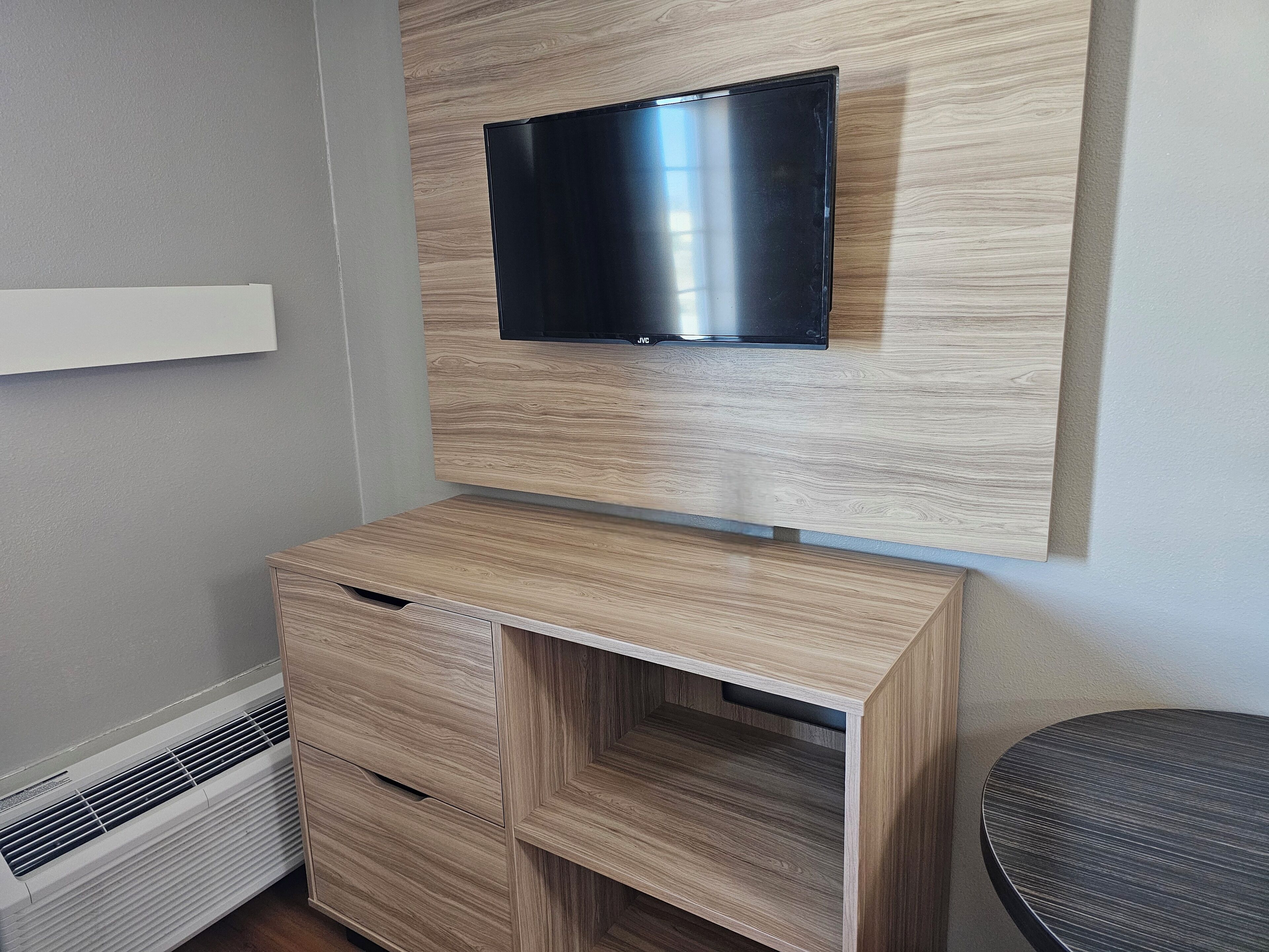 A modern room with a built-in TV on a wooden wall unit, a built-in air conditioner, and a round seating area.