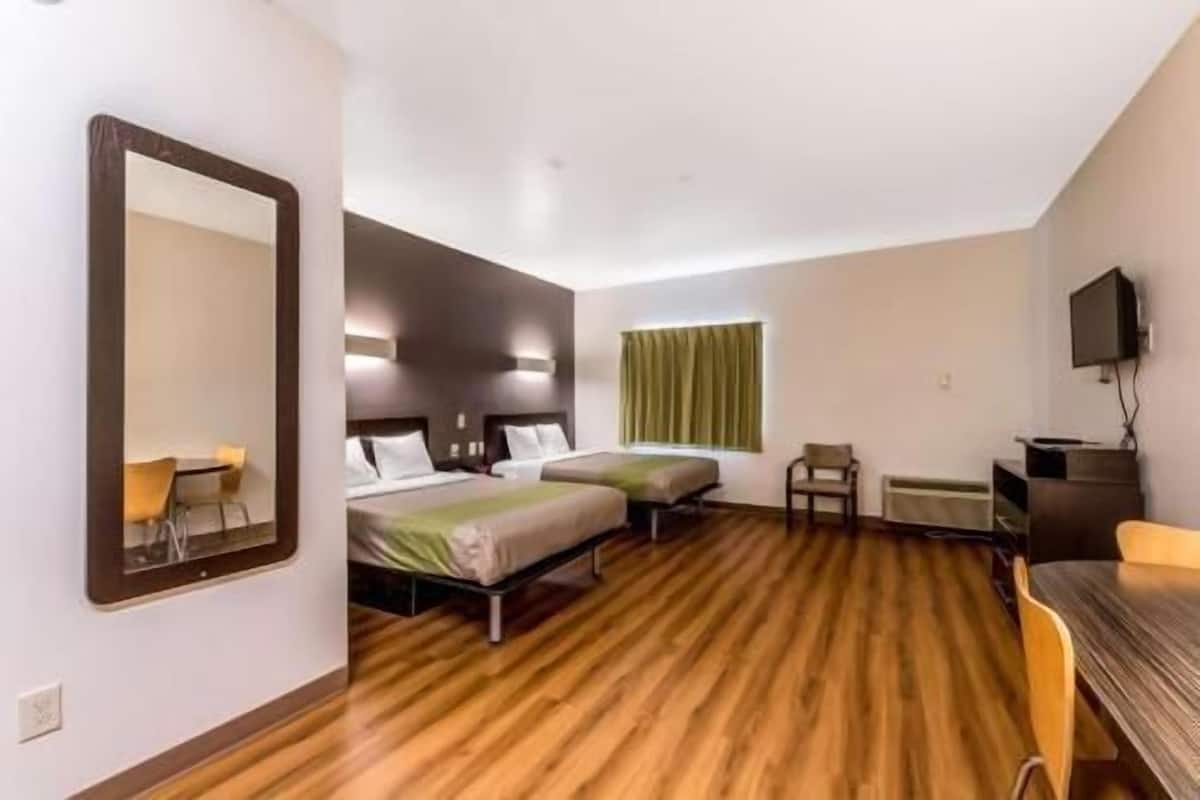 A hotel room with two beds, a desk, a chair, a television, and a window with curtains.