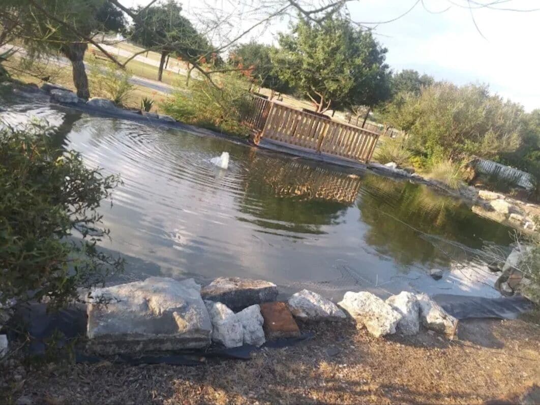 A pond with a wooden deck and a metal railing.