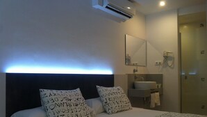 Habitació d'hotel amb llit, almoinades amb dibuixos alfabètics, una taula de nit, un mirall, un lavabo i un telèfon.