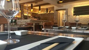 Interior de restaurant amb zona de bar, bigues de fusta al sostre i llums penjants.