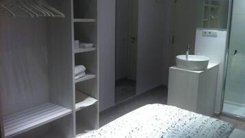 Et soveværelse med seng, walk-in closet, badeværelse med håndvask og spejl, samt brusebad.