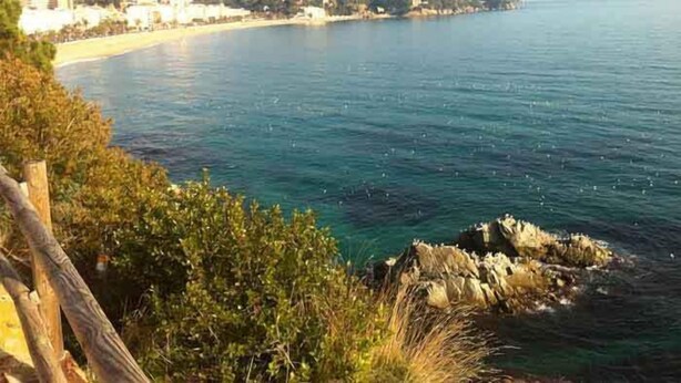 Vista costanera amb una platja, mar blava cristal·lina i un paisatge amb turons al fons.