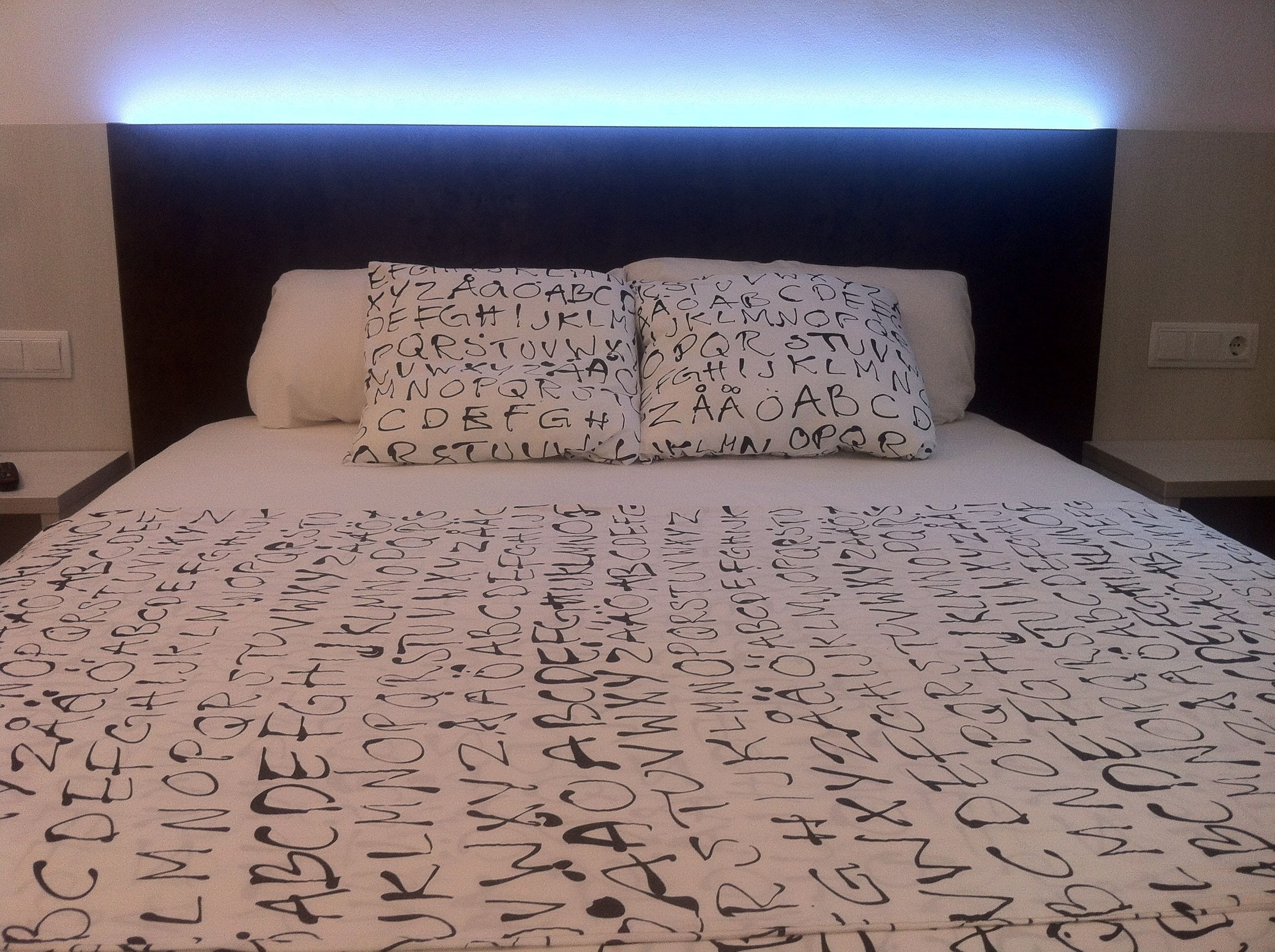 A bed with a white sheet and pillows featuring alphabet patterns.
