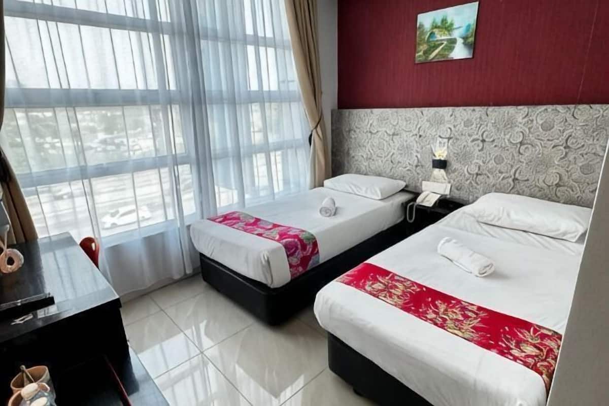 A hotel room with two beds, a desk, and a view through large windows.