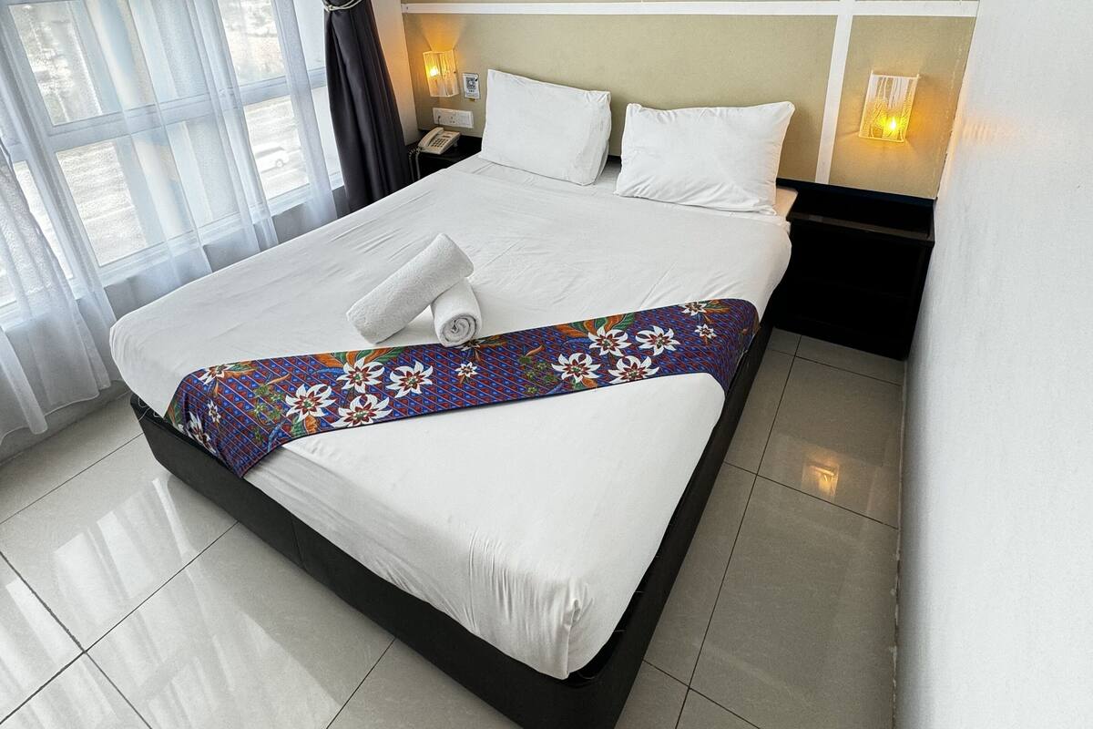 A hotel room with a large bed, a nightstand with a phone, and a window with curtains.