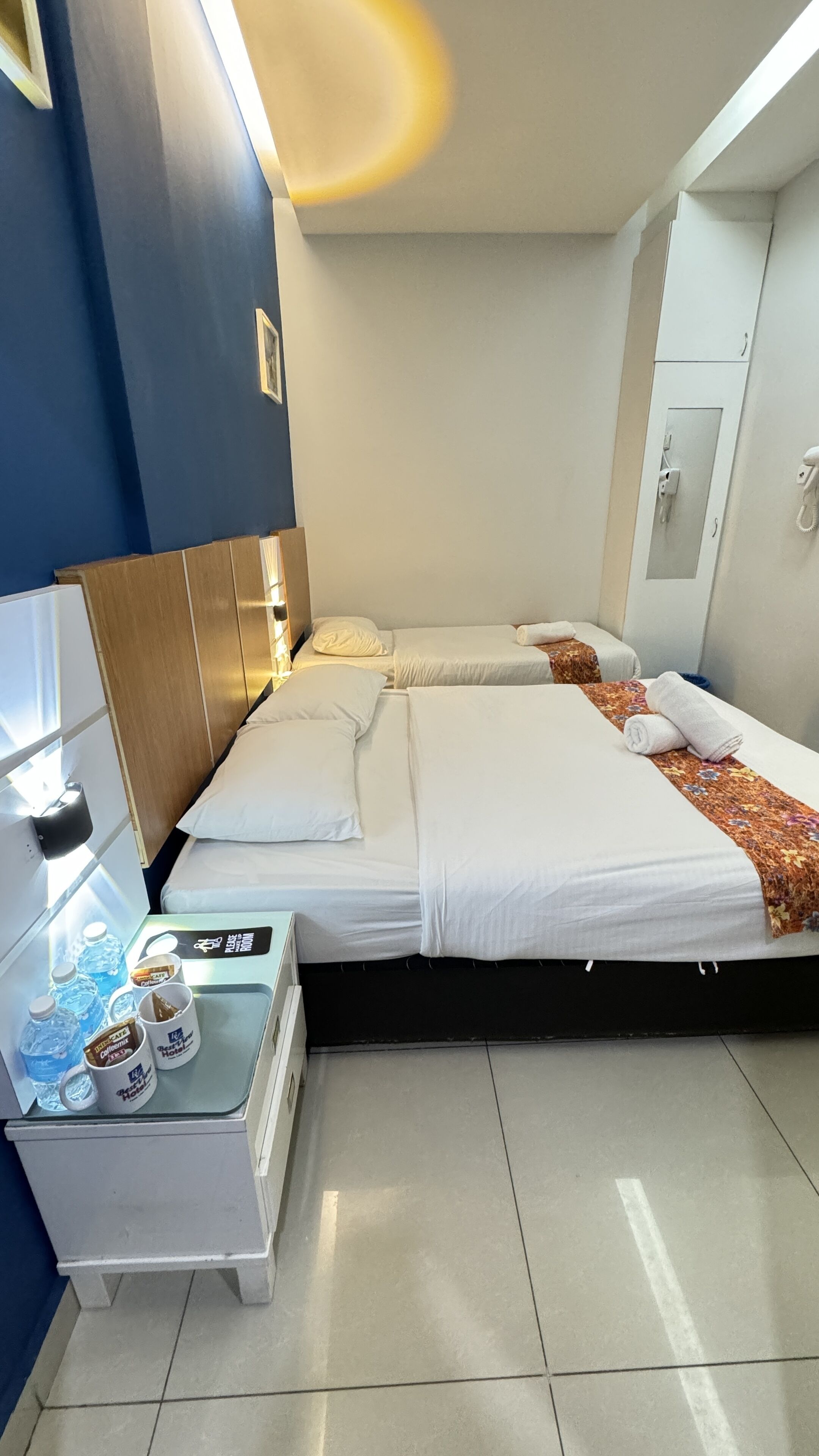 Habitación de hotel con dos camas, un minibar y una pequeña mesa con botellas de agua y tazas de café.