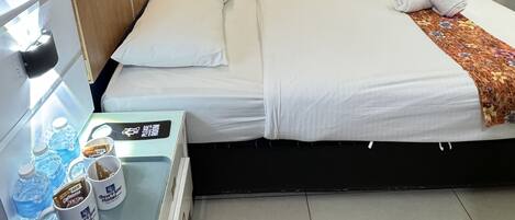 Habitación de hotel con dos camas, un minibar y una pequeña mesa con botellas de agua y tazas de café.
