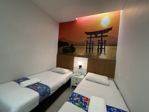 A hotel room with two beds, a nightstand with a lamp, and a wall mural of a sunset over water with a traditional bridge.