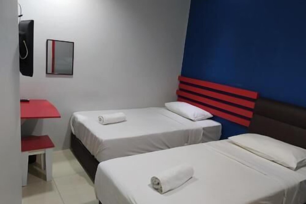 Habitación de hotel con dos camas, un mueble de pared rojo y blanco, y un escritorio pequeño con superficie roja.