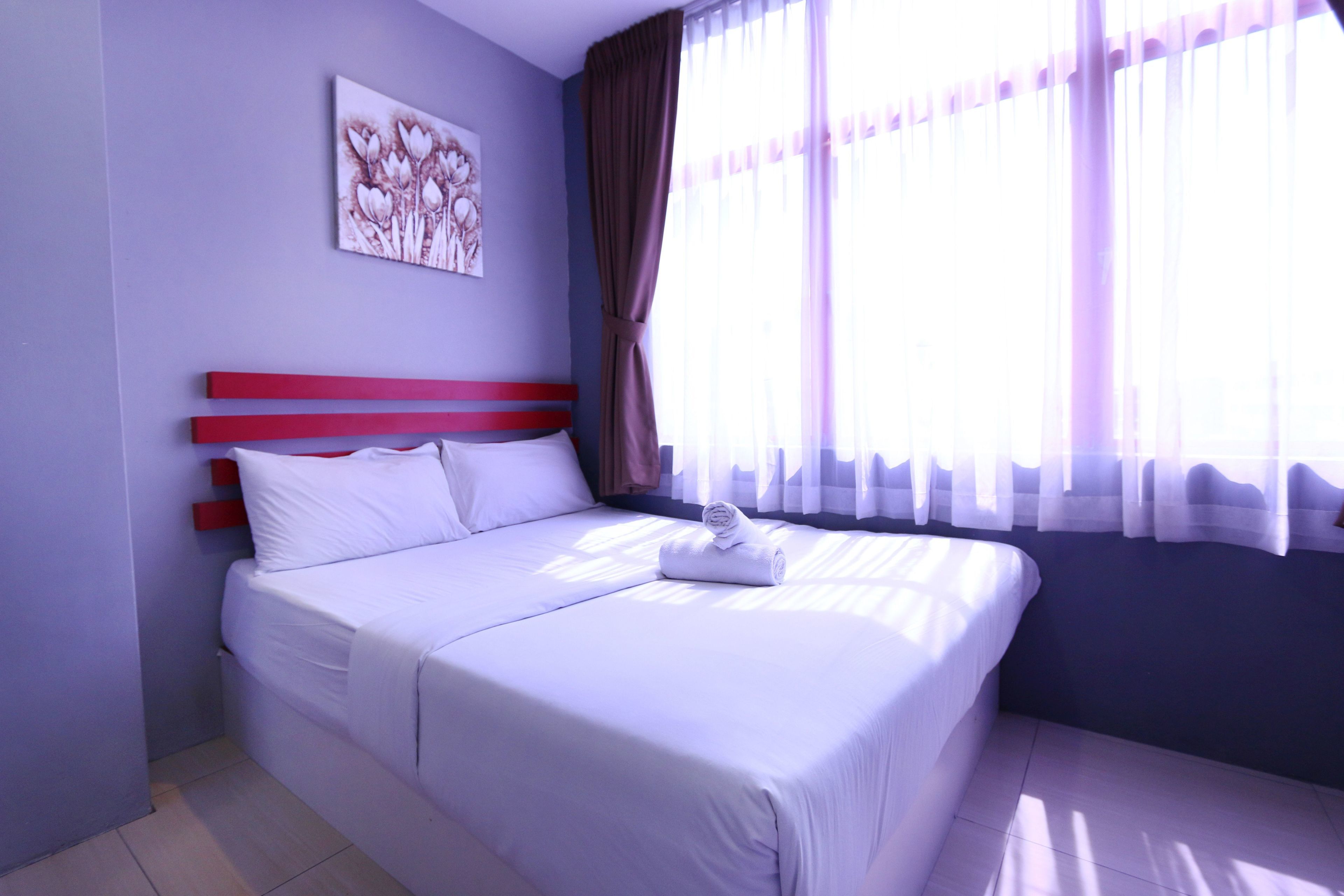 A neatly made bed with white linens, a red headboard, and a wall-mounted artwork.