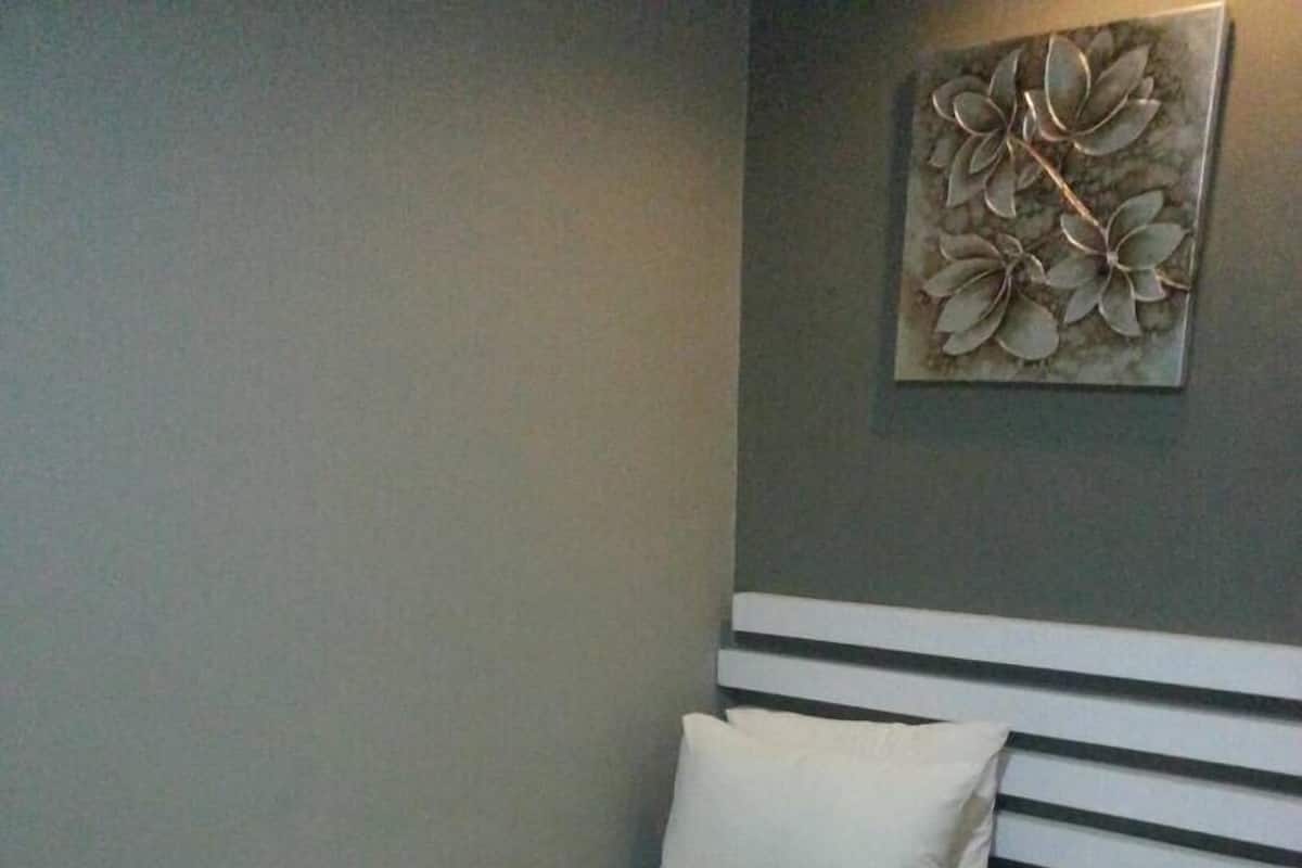 Un lit simple avec une literie blanche, dans une pièce dont un mur est gris et au-dessus duquel on peut voir une œuvre d’art décorative à motifs floraux.