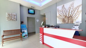 A reception area with a red and white desk, a wooden bench, a wall-mounted TV, and a large plant.