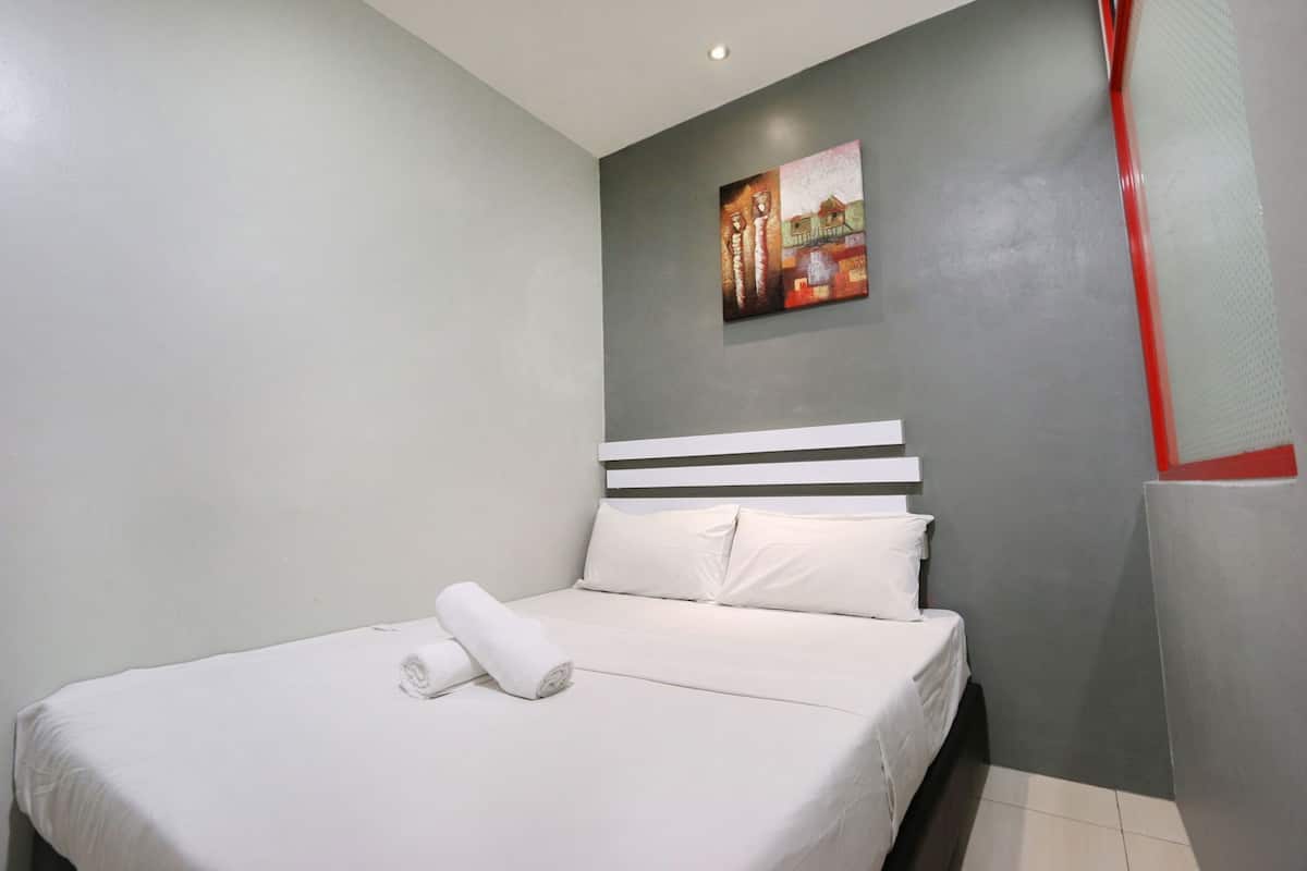 Une chambre d’hôtel avec un lit, du linge de lit blanc, un tableau au mur et un mur d’accent rouge.