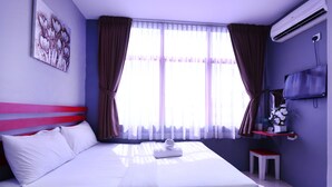 A hotel room with a bed, a TV, a small table, and a window with curtains.