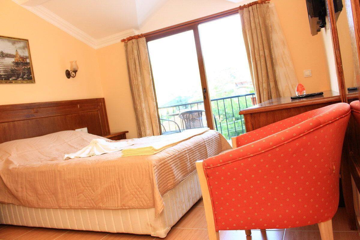 A hotel room with a bed, a red chair, a desk, and a balcony with a view.