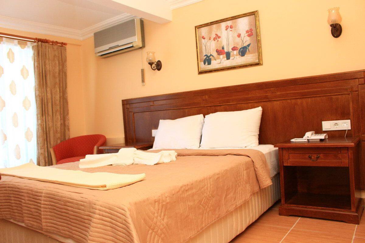A hotel room with a wooden headboard, a bed with white linens, a bedside table with a lamp, and a painting on the wall.