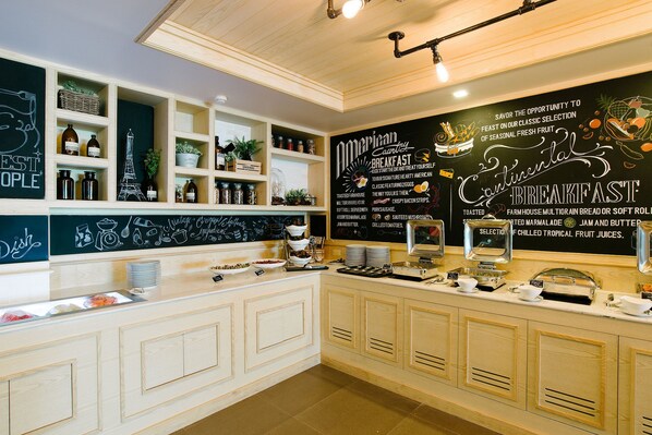 Un espace buffet pour le petit-déjeuner avec un tableau noir affichant le menu, des étagères remplies de condiments et une variété d'aliments pour le petit-déjeuner.