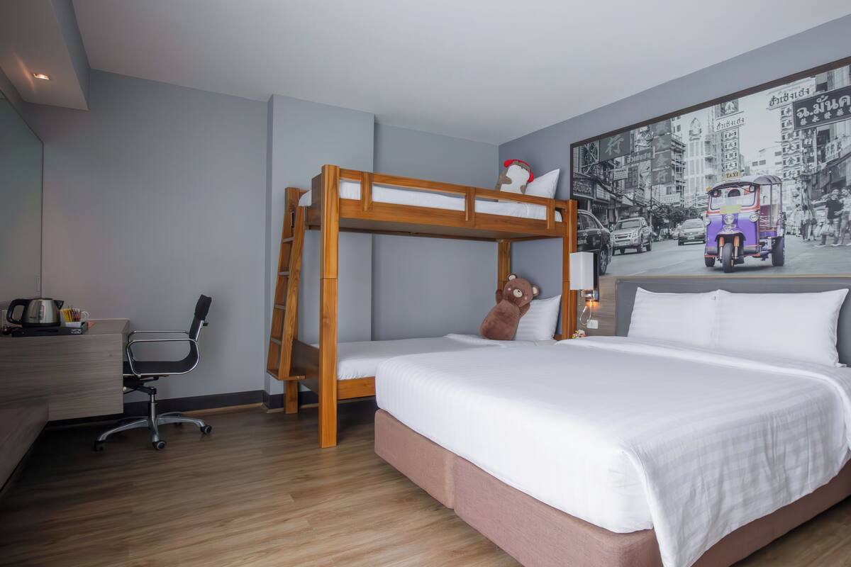 Una habitación de hotel con literas, un escritorio con silla, una lámpara, una mesita de noche y un teléfono montado en la pared.