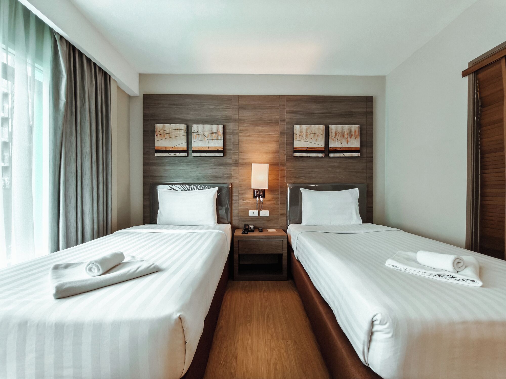 A hotel room with two single beds, a nightstand with a lamp, and artwork on the wall.