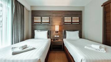 A hotel room with two single beds, a nightstand with a lamp, and artwork on the wall.