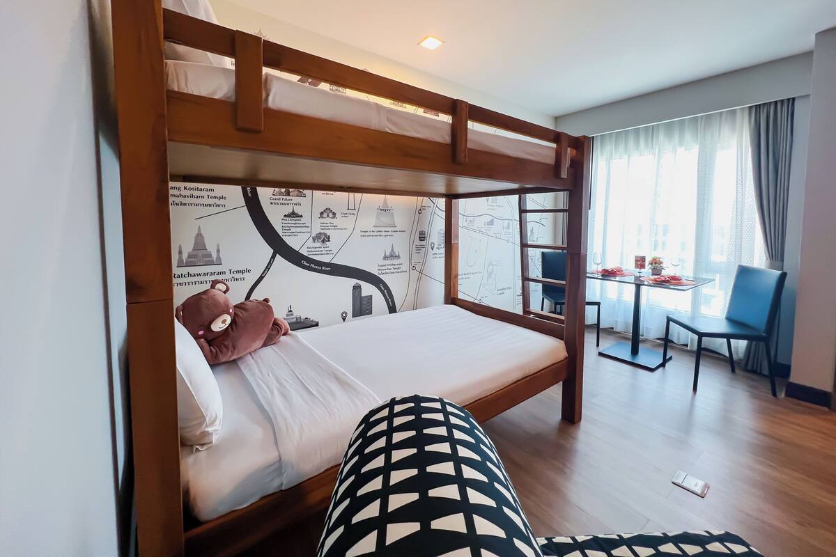 Una cama de literas con un mural de un mapa, una mesa de comedor con sillas y vista de la habitación.