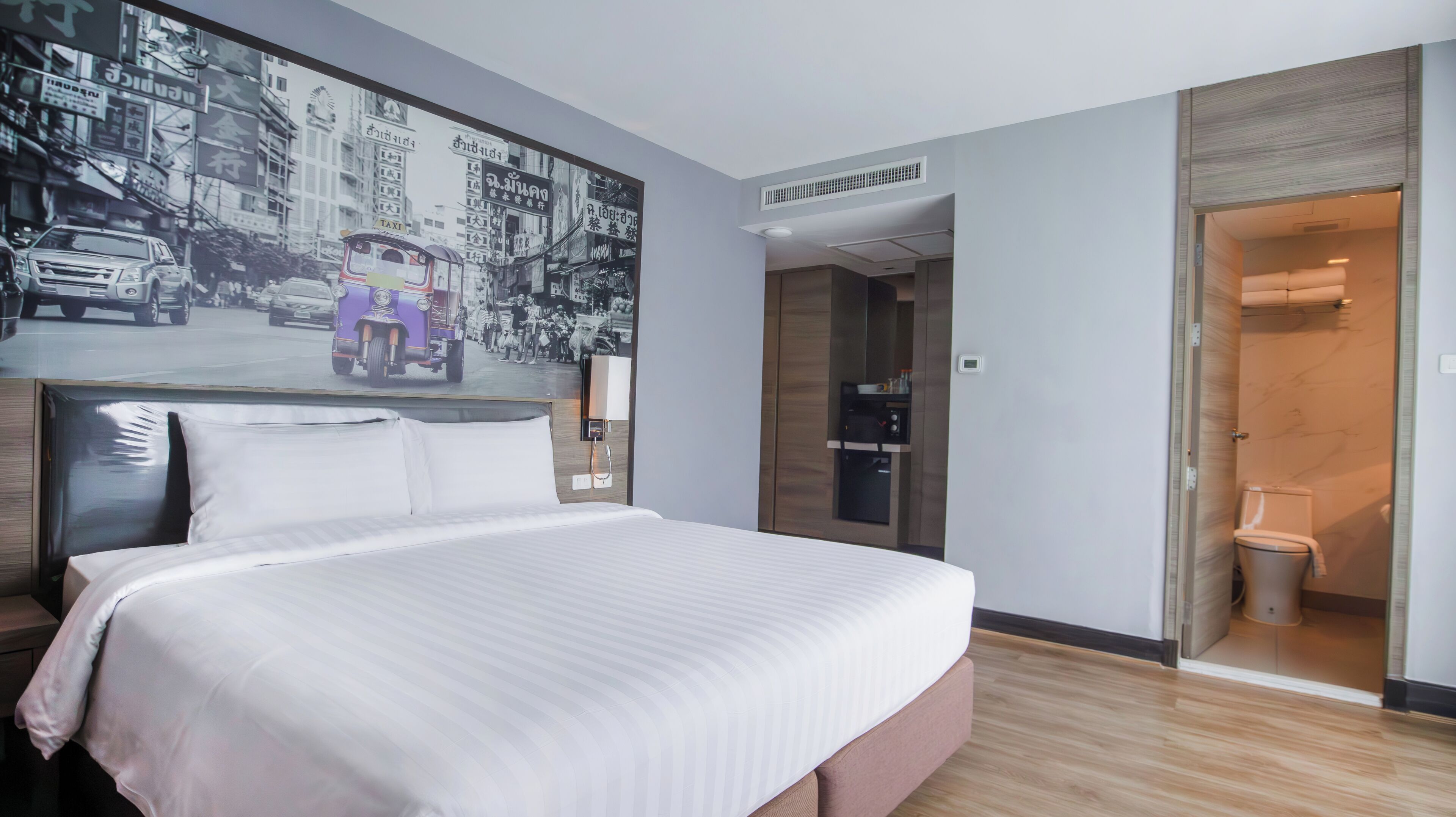 A hotel room with a large bed, a wall-mounted TV, a door leading to a bathroom, and a visible air conditioning unit.