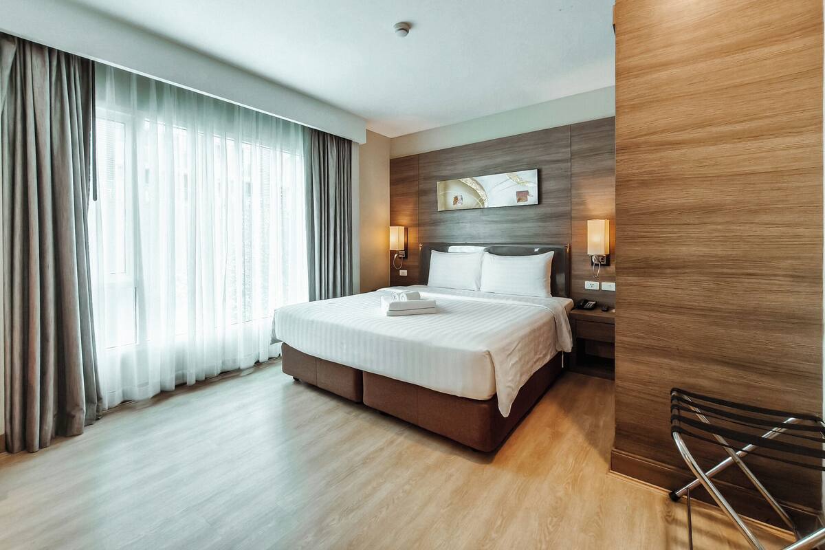 Una habitación de hotel moderna con una cama grande, paneles de madera, vistas a la ciudad y un escritorio con silla.