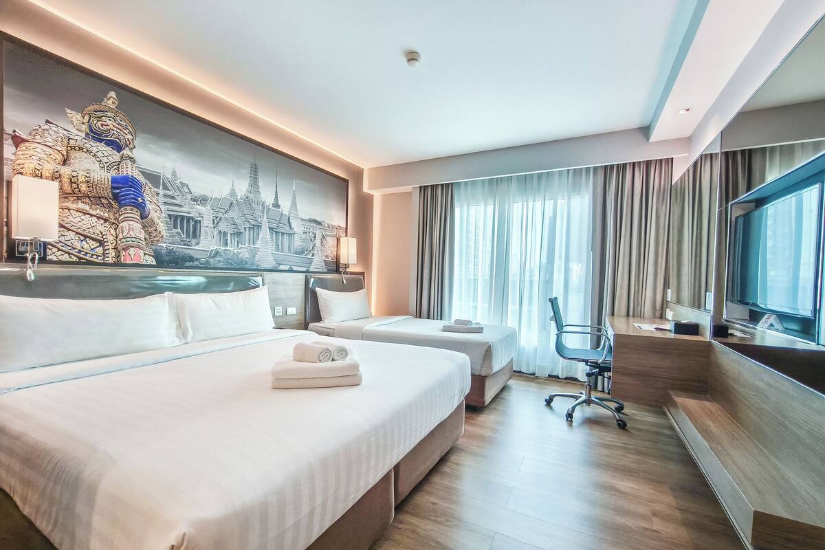 Habitación de hotel con dos camas, un escritorio, una silla, un televisor y un mural grande de un templo.