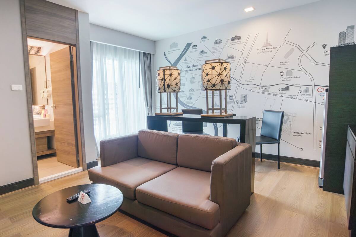 Una habitación de hotel moderna con un sofá, una mesita, un mapa en la pared y una puerta que da a un baño.