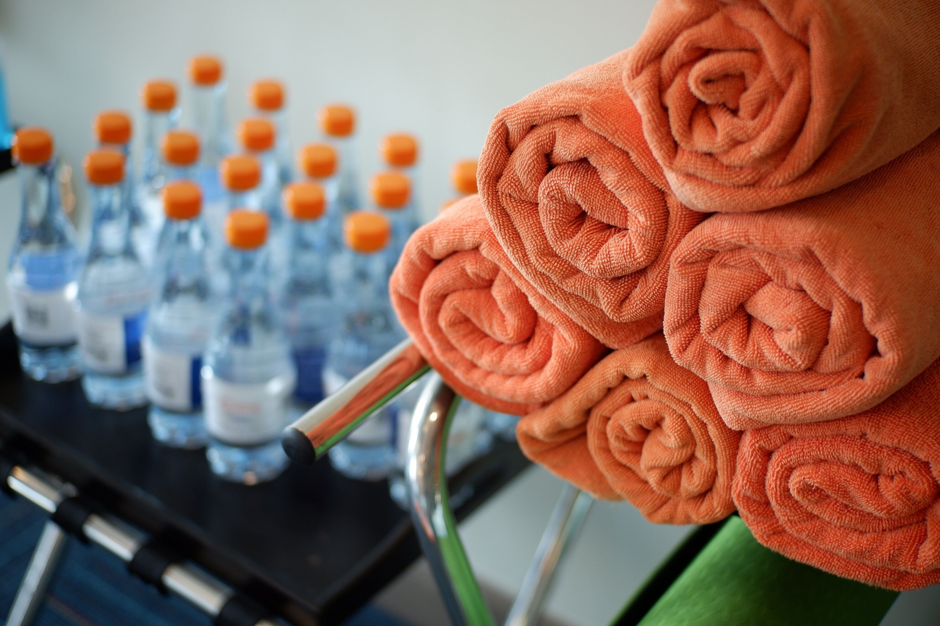 A stack of orange towels and multiple bottles of water on a cart.