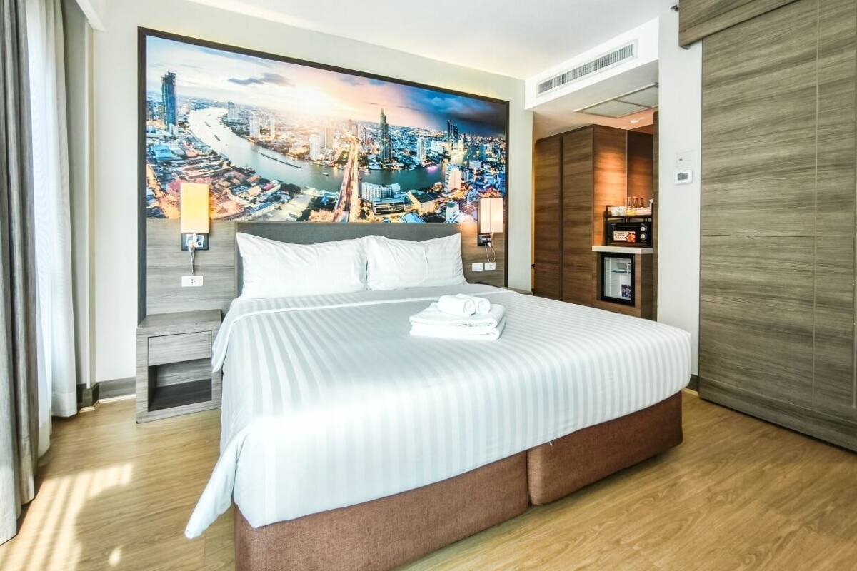 Habitación de hotel con una cama grande, un mural de paisaje urbano en la pared, suelo de madera y un armario con puerta corredera.