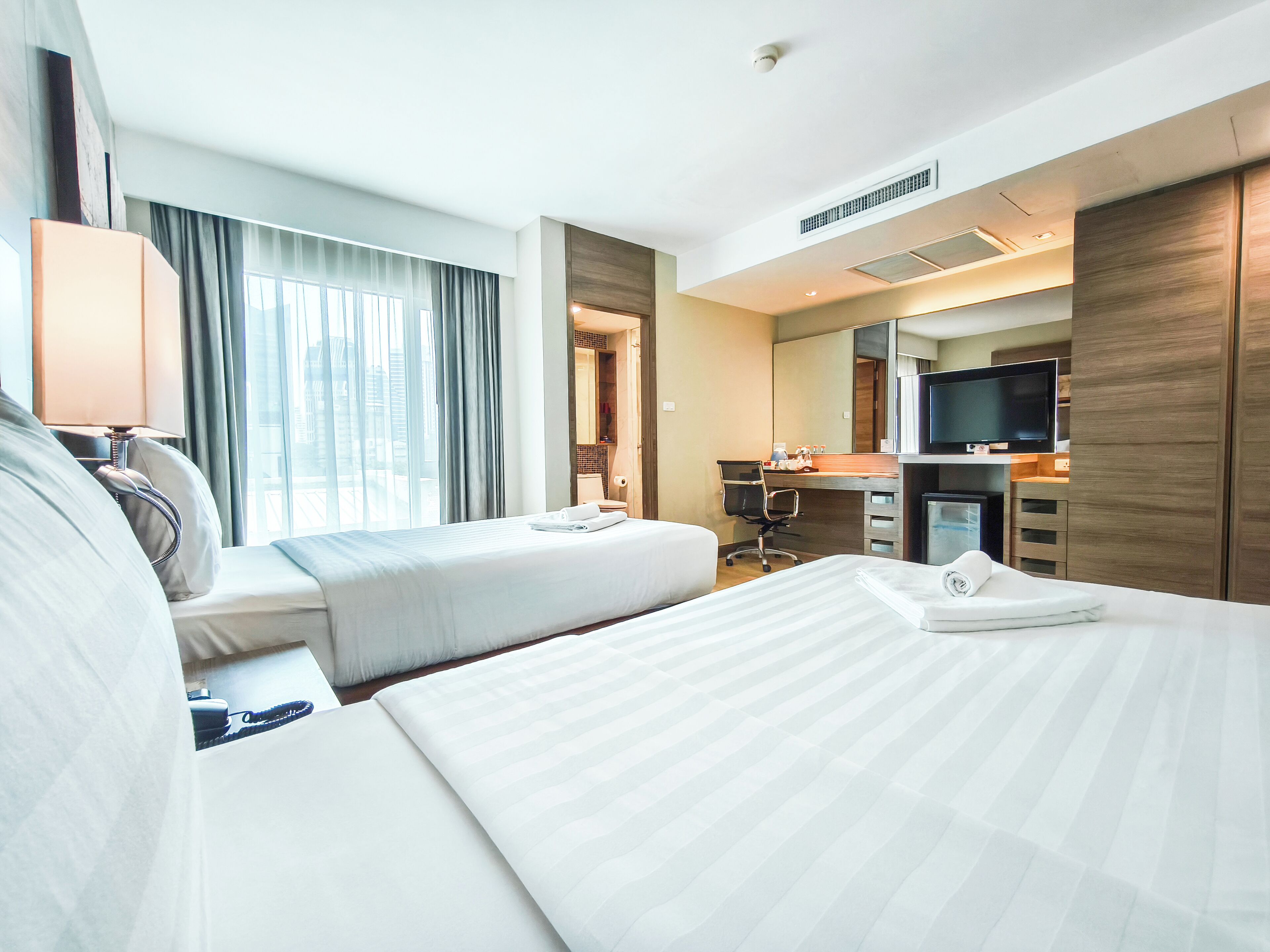 Ein Hotelzimmer mit zwei Betten, einem Schreibtisch, einem Fernseher und einem durch eine offene Tür einsehbaren Badezimmer.