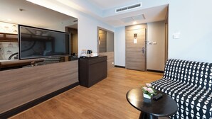 A modern hotel room with a large flat-screen TV, a sofa, a small table with a vase, and a reception desk. - Citrus Sukhumvit 11 Bangkok by Compass Hospitality (Bangkok)