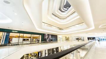 Interior moderno de un centro comercial con un atrio central, barandillas de vidrio y tiendas.