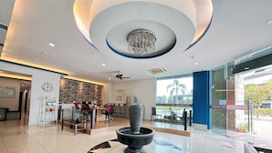 Un moderno vestíbulo de hotel con una fuente central, un mostrador de recepción y un comedor con vistas al exterior.