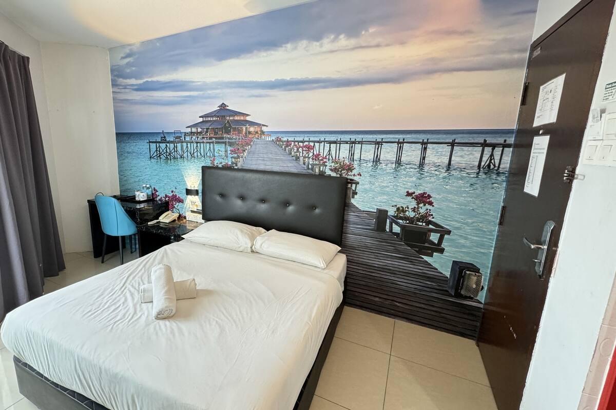 Habitació d'hotel amb un llit, escriptori, cadira i un mural que representa un moll i l'oceà.